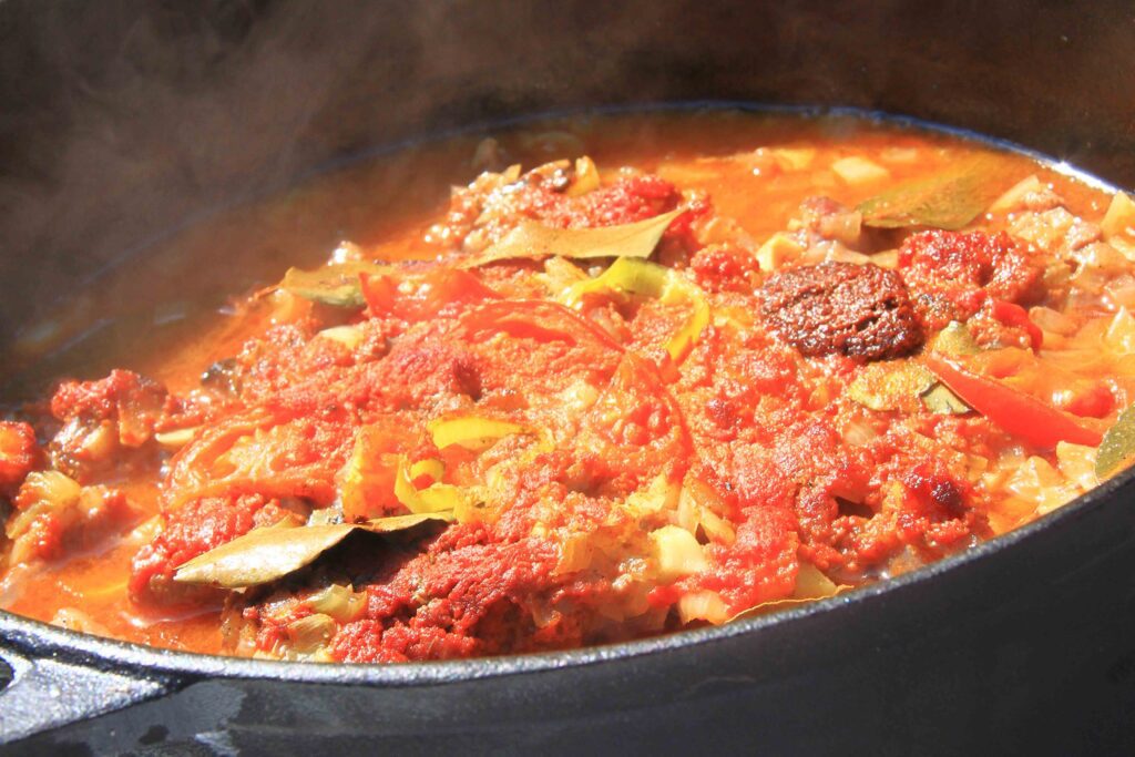 Sűrű, szaftos vadpörkölt öntöttvas edényben, fatüzelésű mobil kemencében lassan összefőzve